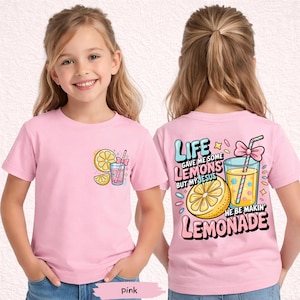 May include: Pink short-sleeved t-shirt with a lemon and lemonade graphic. The front of the shirt features a lemon slice and a glass of lemonade. The back of the shirt has the text "Life gave me some lemons but my Jesus he be makin' lemonade."
