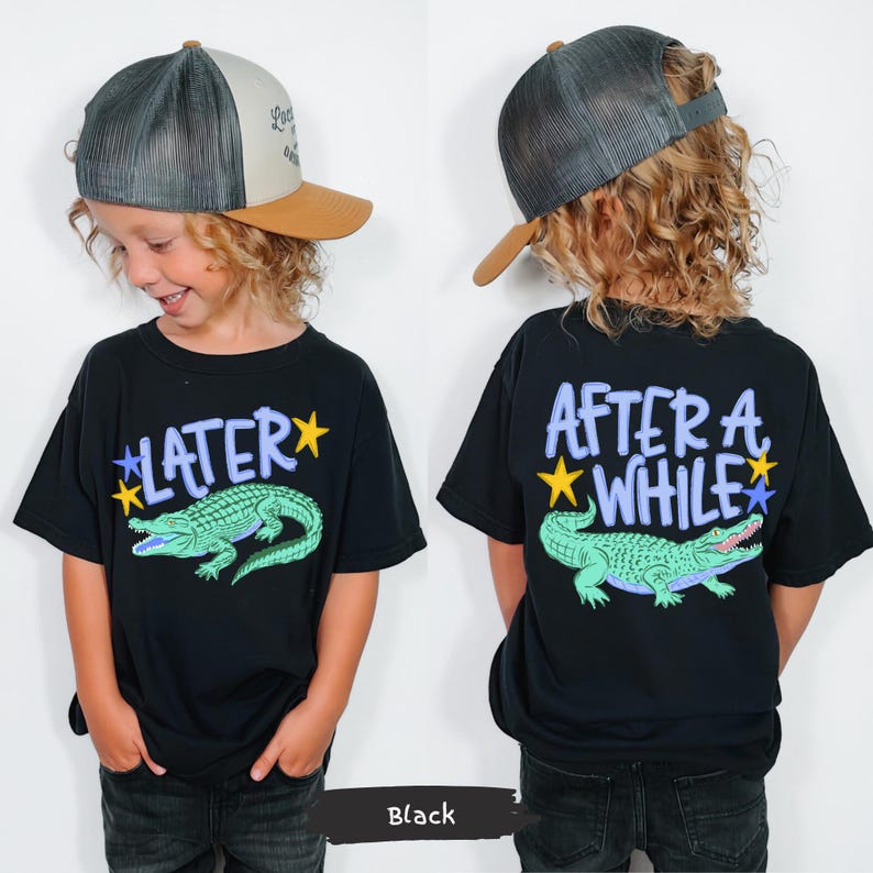 Puede incluir: Camisetas negras con un dise&ntilde;o de cocodrilo de dibujos animados. Una camiseta dice "LATER" con una estrella azul y amarilla, y la otra dice "AFTER A WHILE" con una estrella azul y amarilla. El ni&ntilde;o lleva una gorra de camionero.