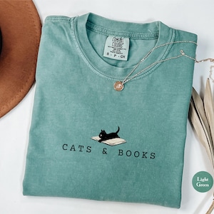 May include: A light green t-shirt with a black cat reading a book and the text "Cats & Books".