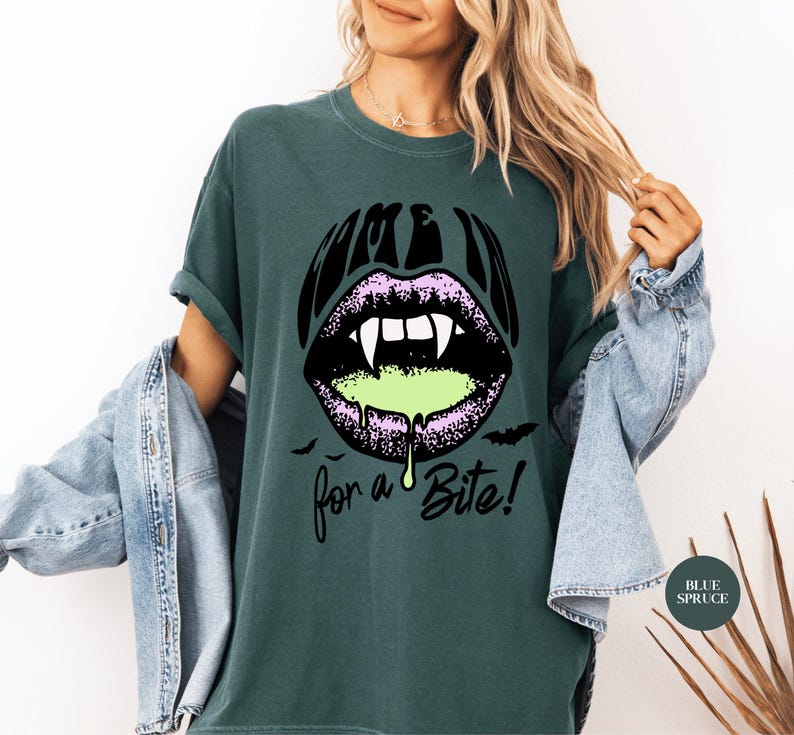 May include: A dark spruce green t-shirt featuring a graphic of black lips with white fangs and dripping neon green liquid. The text reads "COME IN" above the lips and "for a Bite!" below, accompanied by small black bat silhouettes.