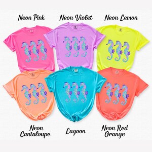 May include: Six colorful t-shirts in neon shades of pink, violet, lemon, cantaloupe, lagoon, and red-orange. Each shirt features a seahorse design in shades of blue, purple, and green. The names of the colors are printed above the shirts.