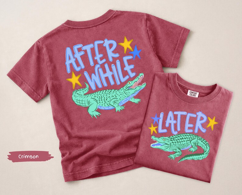 Puede incluir: Dos camisetas carmes&iacute; con gr&aacute;ficos de caimanes. Una camiseta dice "AFTER WHILE" con un caim&aacute;n verde y estrellas amarillas y azules. La otra camiseta dice "LATER" con un caim&aacute;n verde y estrellas amarillas y azules.