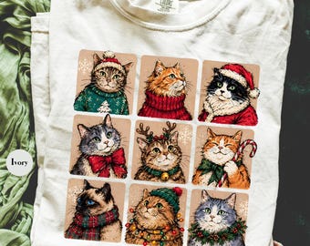 May include: An ivory t-shirt featuring a grid of nine illustrations of cats dressed in holiday attire, including sweaters, scarves, Santa hats, reindeer antlers, and Christmas lights, with a Comfort Colors brand label at the inner neckline.