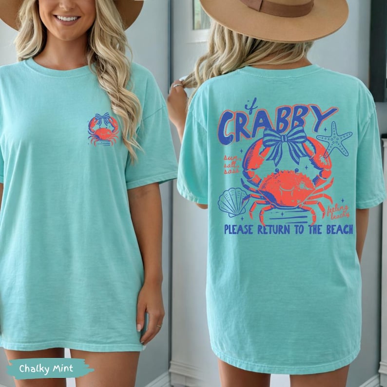Puede incluir: Una camiseta turquesa con un gr&aacute;fico de cangrejo. La parte delantera presenta un peque&ntilde;o dise&ntilde;o de cangrejo, mientras que la parte trasera muestra una ilustraci&oacute;n de cangrejo m&aacute;s grande con el texto "If Crabby, Please Return to the Beach". La camiseta es de corte holgado.