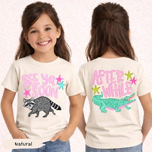 May include: A natural-colored t-shirt with the text "SEE YA SOON" and a raccoon graphic on the front. The back of the shirt features the text "AFTER WHILE" and a crocodile graphic. Pink and teal accents.