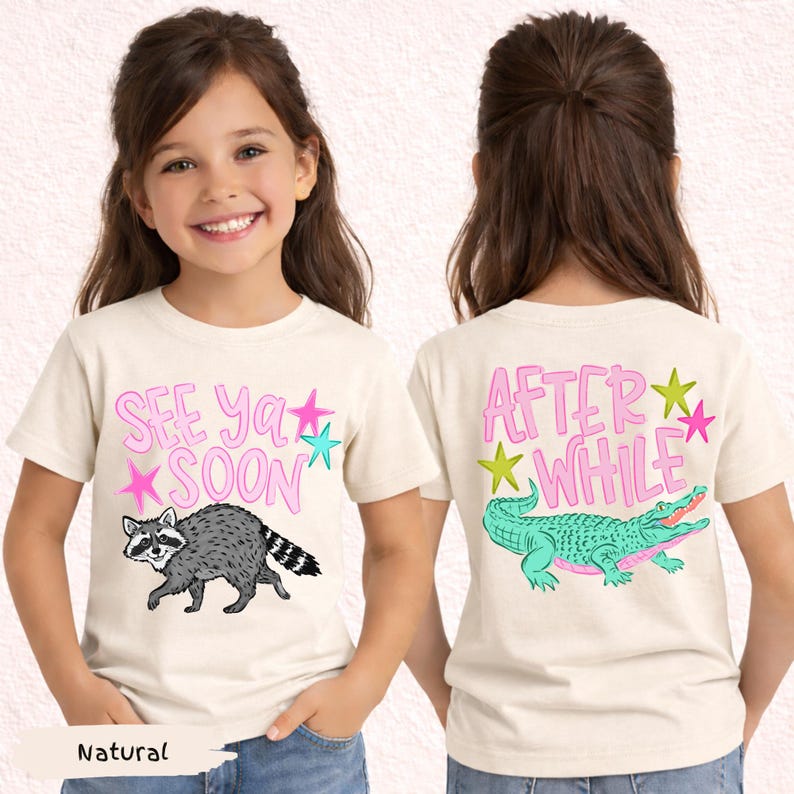 May include: A natural-colored t-shirt with the text "SEE YA SOON" and a raccoon graphic on the front. The back of the shirt features the text "AFTER WHILE" and a crocodile graphic. Pink and teal accents.
