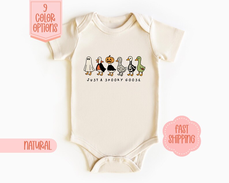 May include: A cream-coloured baby bodysuit featuring a Halloween-themed graphic. The design shows cartoon geese dressed as a ghost, a witch, a pumpkin, a mummy, and a zombie. Text reads "JUST A SPOOKY GOOSE".