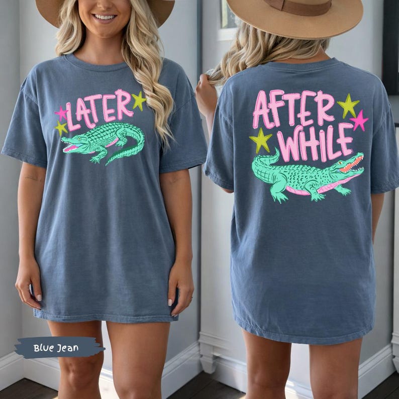 May include: Blue jean colored t-shirt with a front graphic that says "LATER" with a pink star and a green alligator. The back of the shirt says "AFTER WHILE" with a green alligator and pink and yellow stars. The shirt is a casual style.