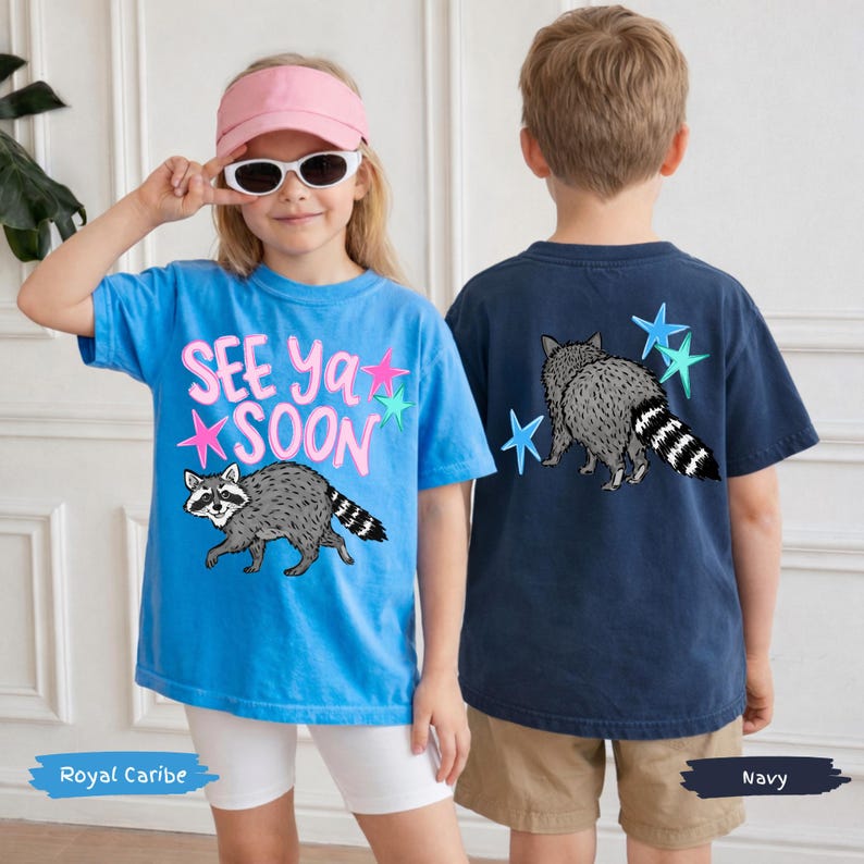 May include: Two children wearing t-shirts with raccoon graphics. One shirt is royal blue with the text "SEE YA SOON" and pink and blue stars. The other shirt is navy blue with a raccoon and blue stars.