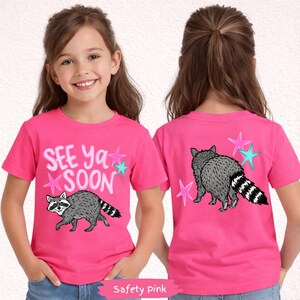 May include: Safety pink t-shirt with a raccoon graphic and the text "See Ya Soon". The raccoon is gray with a black and white striped tail. Pink and teal stars surround the text and raccoon.