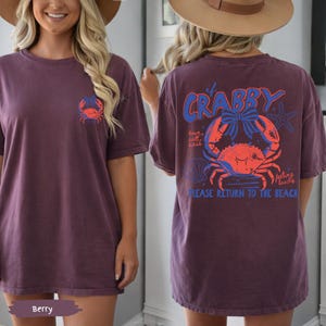 Puede incluir: Camiseta de color bayas con un gr&aacute;fico de cangrejo en la parte delantera y trasera. La parte trasera de la camiseta presenta el texto "It's Crabby" encima de una ilustraci&oacute;n de cangrejo, con las palabras "sun, salt, sass" y "feeling beachy" y "PLEASE RETURN TO THE BEACH".