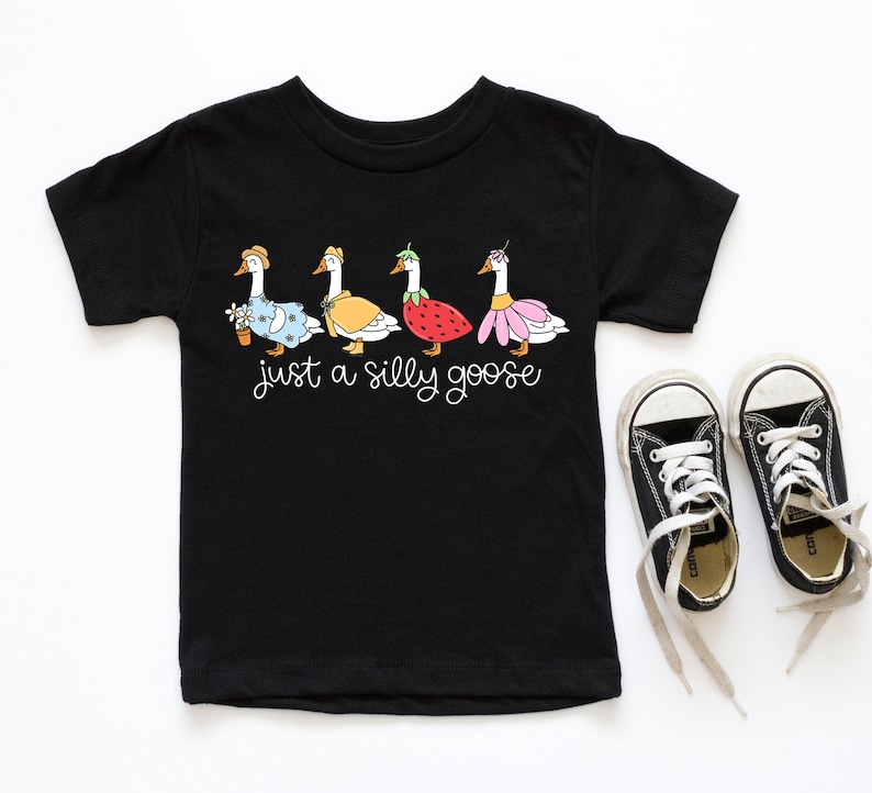 以下が含まれることがあります： 黒い半袖Tシャツに、異なる衣装を着た5羽のガチョウと「Just a silly goose」というテキストのグラフィックがプリントされています。