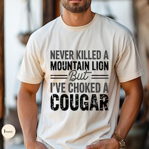 May include: A white t-shirt with a black graphic that reads "Never killed a mountain lion but I've choked a cougar".