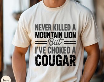 May include: A white t-shirt with a black graphic that reads "Never killed a mountain lion but I've choked a cougar".