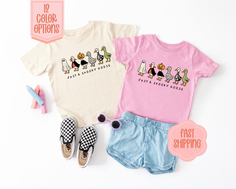 May include: Two children's t-shirts, one cream and one pink, with a Halloween goose design. The shirts feature cartoon geese dressed as a ghost, a witch, a pumpkin, and a mummy. Text reads "JUST A SPOOKY GOOSE".