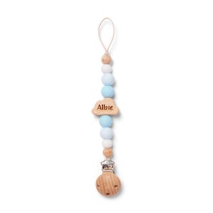 May include: A baby pacifier clip with a wooden cloud charm engraved with the name "Albie". The clip features a string of light blue, white, and wooden beads, and a wooden clip at the bottom.