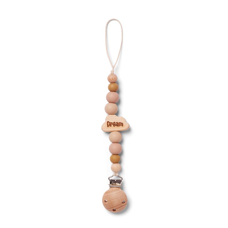 May include: A wooden pacifier clip with a string loop. The clip features a series of wooden beads in shades of pink and brown. A cloud-shaped charm with the word "Dream" is attached. The clip has a silver-colored metal clasp.