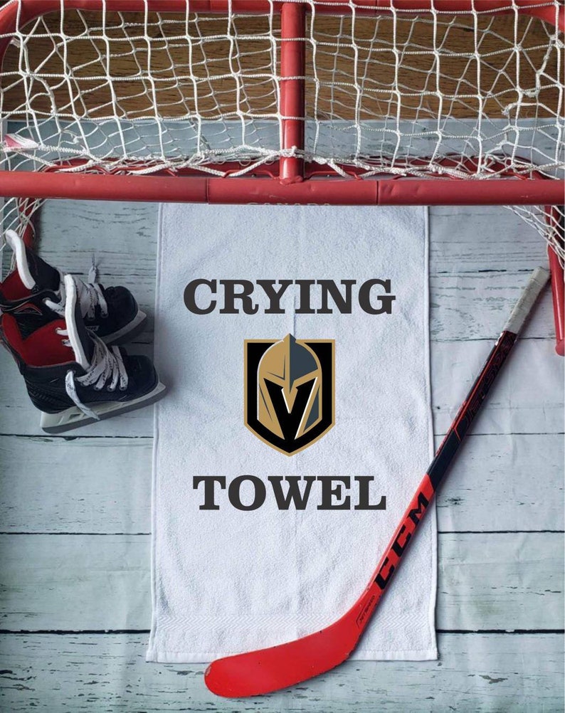 Peut inclure: Une serviette blanche avec les mots "Crying Towel" et un logo d'&eacute;quipe, un b&acirc;ton de hockey rouge et une paire de patins &agrave; glace sont affich&eacute;s pr&egrave;s d'un but de hockey. La serviette est centr&eacute;e, avec le b&acirc;ton de hockey et les patins de chaque c&ocirc;t&eacute;.