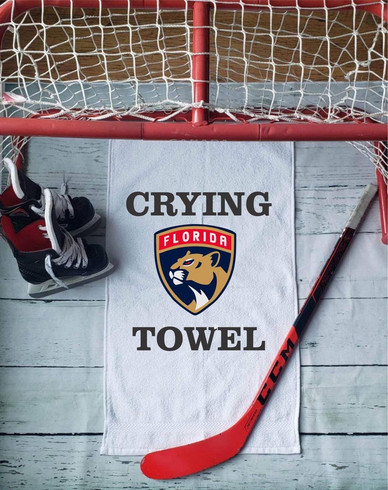 Peut inclure: Une serviette blanche avec le texte "Crying Towel" et le logo des Panthers de la Floride, un b&acirc;ton de hockey rouge et des patins &agrave; glace sont dispos&eacute;s pr&egrave;s d'un but de hockey.