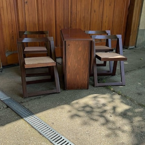 Peut inclure: Un ensemble de table pliante et deux chaises en bois brun foncé. Les chaises ont des assises tissées. La table est pliée et compacte. L'ensemble est en bois. Idéal pour les petits espaces.
