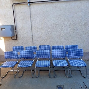 Puede incluir: Un conjunto de diez sillas vintage con marcos cromados. Los asientos y respaldos están tapizados en tela a cuadros azul y blanco. Las sillas están dispuestas en fila, adecuadas para un comedor o cocina.