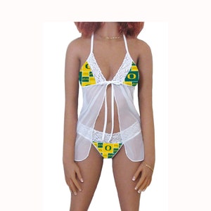 May include: White lace lingerie with a green and yellow checkered pattern featuring a large letter "O" in the center. The lingerie has a halter top and a matching bottom.