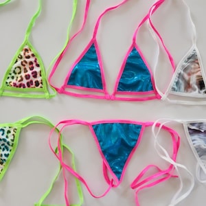 May include: A collection of colorful bikinis. Styles include neon green trim with leopard print, bright pink trim with shiny blue fabric, and white trim with a watercolor design. Each bikini has matching tops and bottoms.
