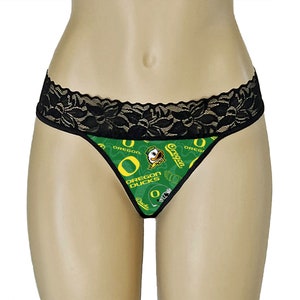 May include: Green and yellow Oregon Ducks thong underwear with a black lace trim. The underwear features the Oregon Ducks logo and text on a green background. The design includes the team's mascot, a duck.