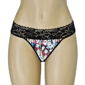 May include: Black thong underwear with a black lace trim. The front panel features a colorful print of characters from The Nightmare Before Christmas, including Sally and Jack Skellington.
