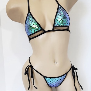 May include: A black and blue bikini with a mermaid scale pattern. The top is a triangle style with adjustable straps and the bottom is a cheeky style with ties on the sides.