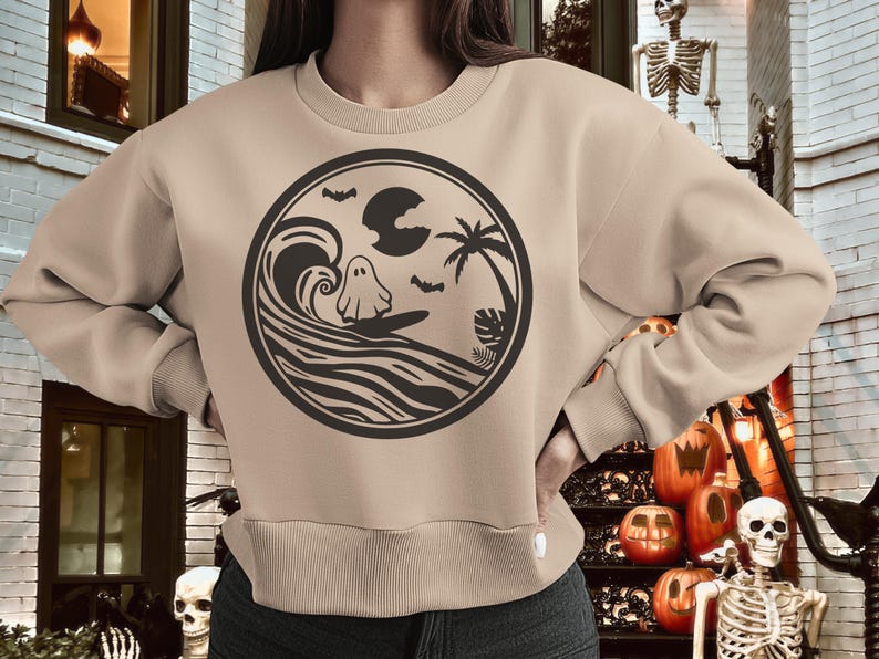 May include: A tan sweatshirt with a black graphic of a ghost surfing on a wave with a palm tree and a moon in the background.