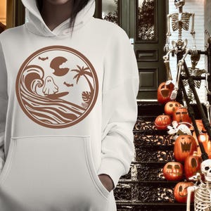 May include: White hoodie with a brown graphic of a ghost surfing on a wave with palm trees and bats. The graphic is in a circle.