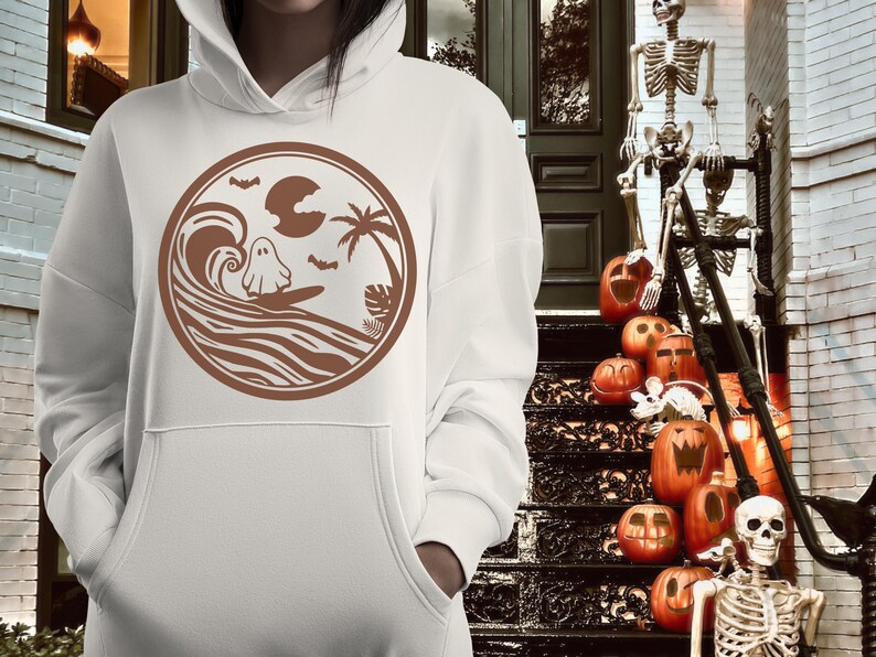 May include: White hoodie with a brown graphic of a ghost surfing on a wave with palm trees and bats. The graphic is in a circle.