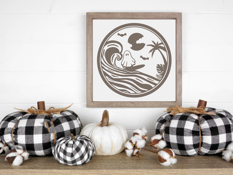 May include: A framed print with a black and white illustration of a ghost surfing on a wave with a palm tree and a full moon in the background. The print is surrounded by black and white checkered pumpkins and cotton bolls.