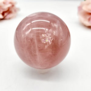 May include: A large, polished rose quartz sphere with a pink hue and iridescent inclusions. The sphere is smooth and reflective, with visible striations in the stone.