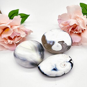 May include: Three white agate stones with gray and black patterns. The stones are smooth and polished.