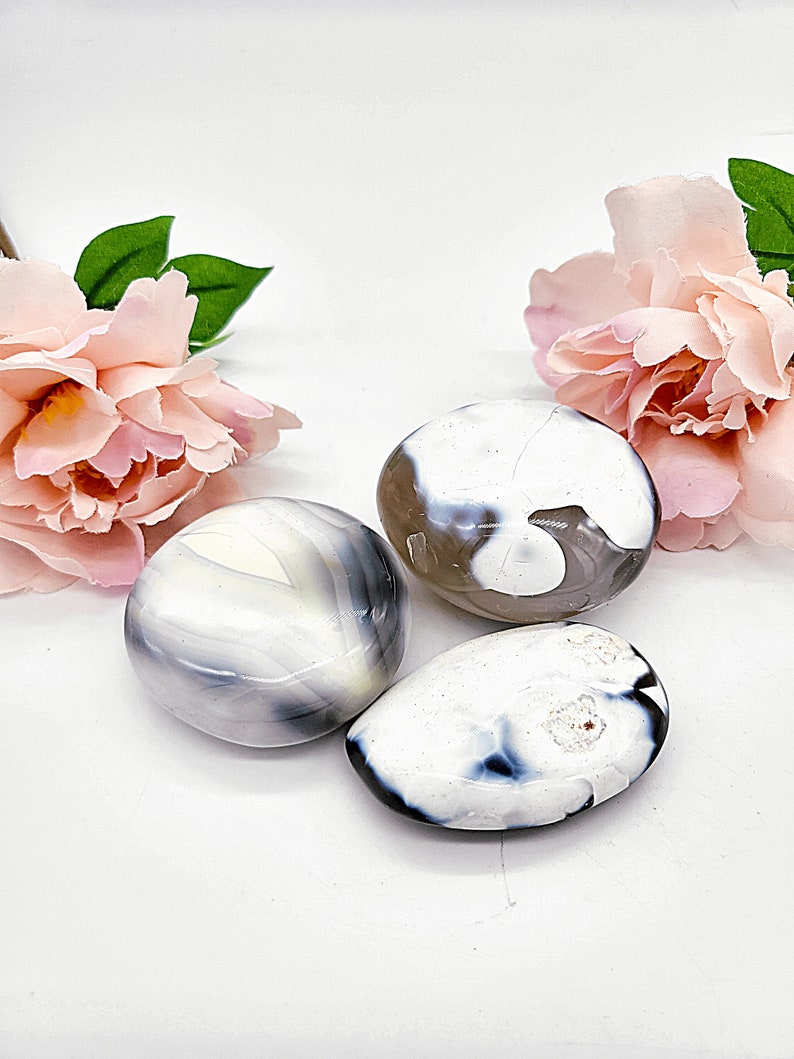 May include: Three white agate stones with gray and black patterns. The stones are smooth and polished.