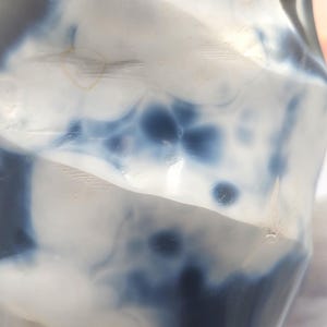 May include: A polished, irregularly shaped stone with a marbled appearance. The stone features a mix of white and deep blue hues, creating a swirling pattern. The surface is smooth and reflective, with subtle variations in color intensity.