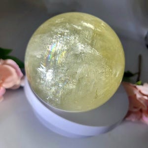 May include: A large, yellow, crystal sphere with iridescent rainbow flashes. The sphere is sitting on a white, circular base.