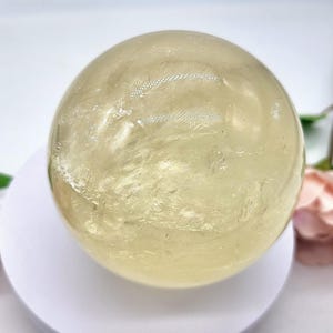 May include: A large, smooth, yellow citrine sphere on a white stand. The sphere has a translucent, glassy appearance with subtle internal striations.