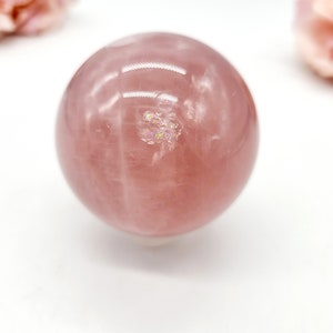 May include: A large, polished rose quartz sphere with a pink hue and iridescent inclusions. The sphere is smooth and reflective, with a slight sheen.