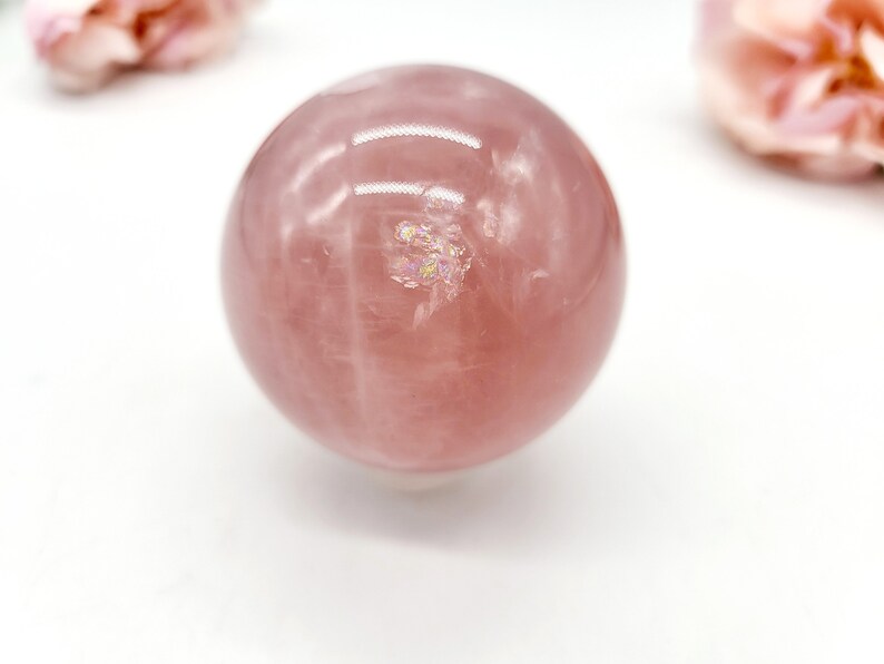 May include: A large, polished rose quartz sphere with a pink hue and iridescent inclusions. The sphere is smooth and reflective, with a slight sheen.