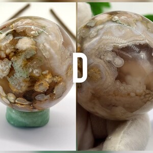 May include: A polished agate sphere with a brown, white and green pattern. The sphere is sitting on a green base.