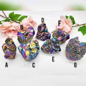 May include: Seven iridescent rainbow aura quartz crystal clusters, labelled A to G. The crystals are various sizes and shapes, with a dark purple, blue, and gold colour.