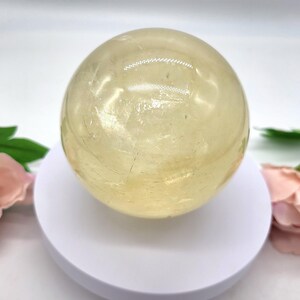 May include: A large, smooth, yellow citrine sphere on a white stand. The sphere is polished and has a translucent appearance.