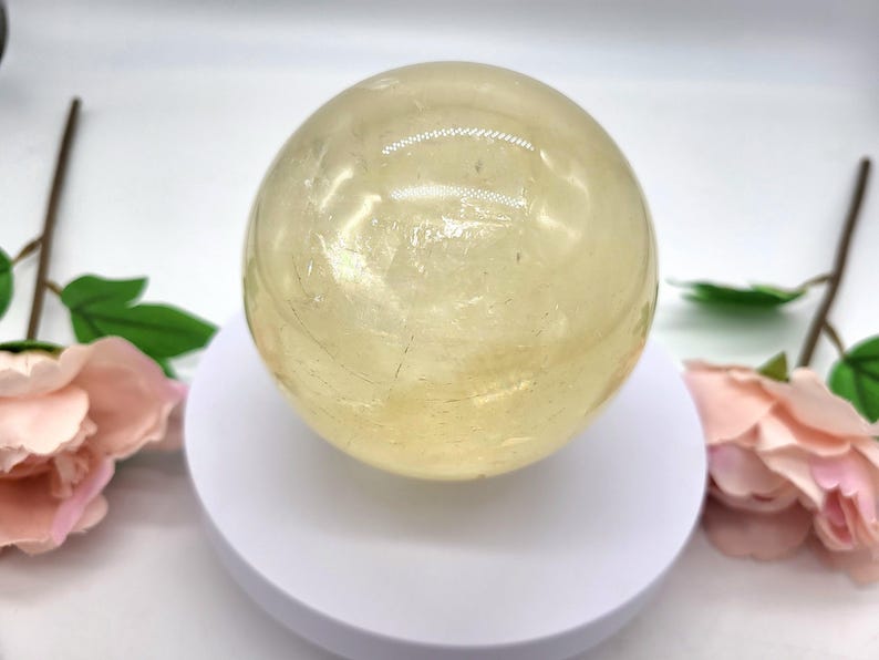 May include: A large, smooth, yellow citrine sphere on a white stand. The sphere is polished and has a translucent appearance.
