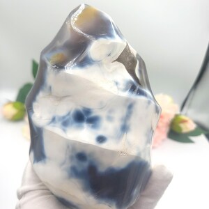 May include: A polished, freeform agate stone with a mix of white, navy blue, and tan colors. The stone has a smooth, glossy surface and a unique, organic shape. This decorative stone is ideal for home decor or as a unique gift.