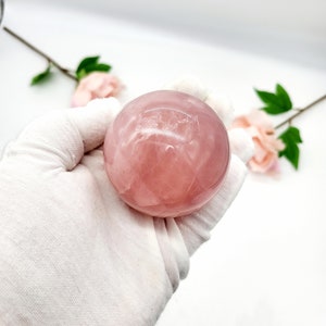 May include: A smooth, pink rose quartz sphere. The sphere is polished and has a translucent appearance.