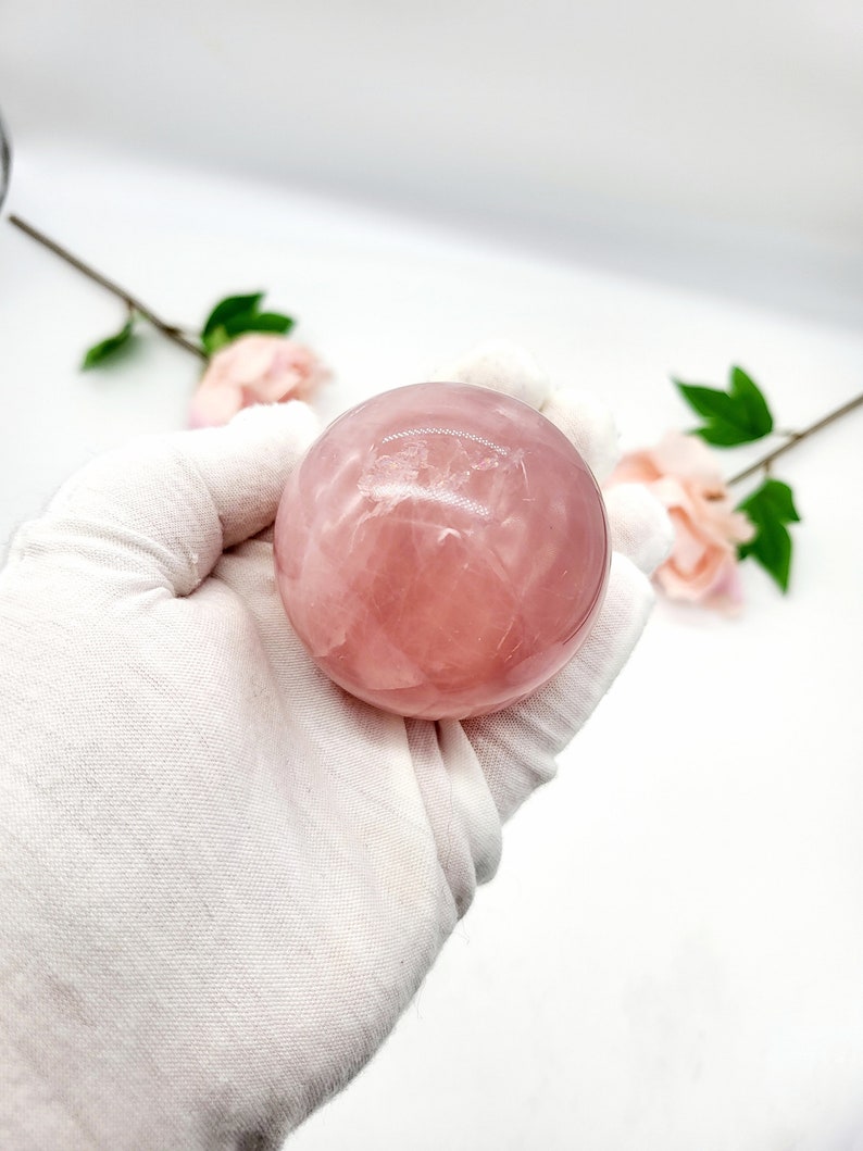 May include: A smooth, pink rose quartz sphere. The sphere is polished and has a translucent appearance.