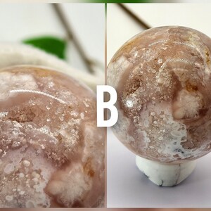 May include: A close-up of a pink and white agate sphere with a white base. The sphere has a unique pattern of white and brown markings.